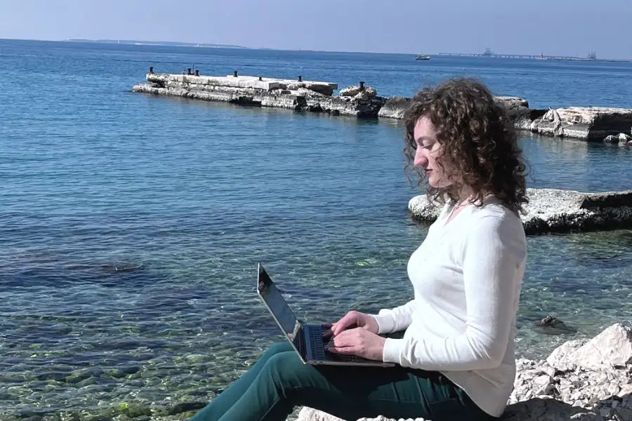 Content Specialist Maria Grazia De Falco che lavora con il computer sugli scogli in riva al mare