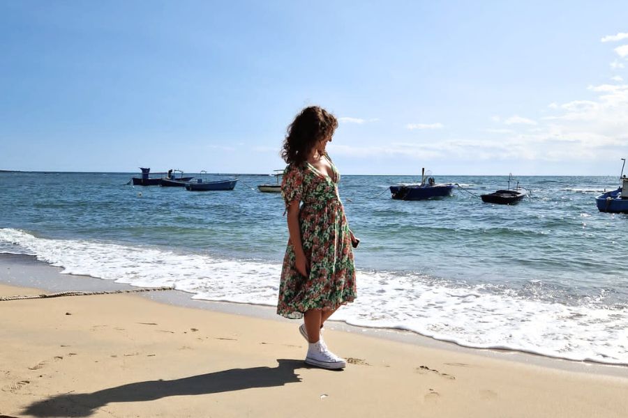 Ragazza con abito floreale che cammina in spiaggia con lo sfondo del mare