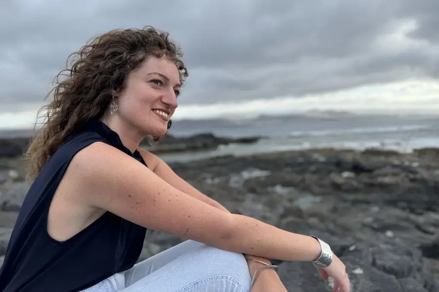 ragazza seduta su uno scoglio che guarda il cielo. il mare sullo sfondo.